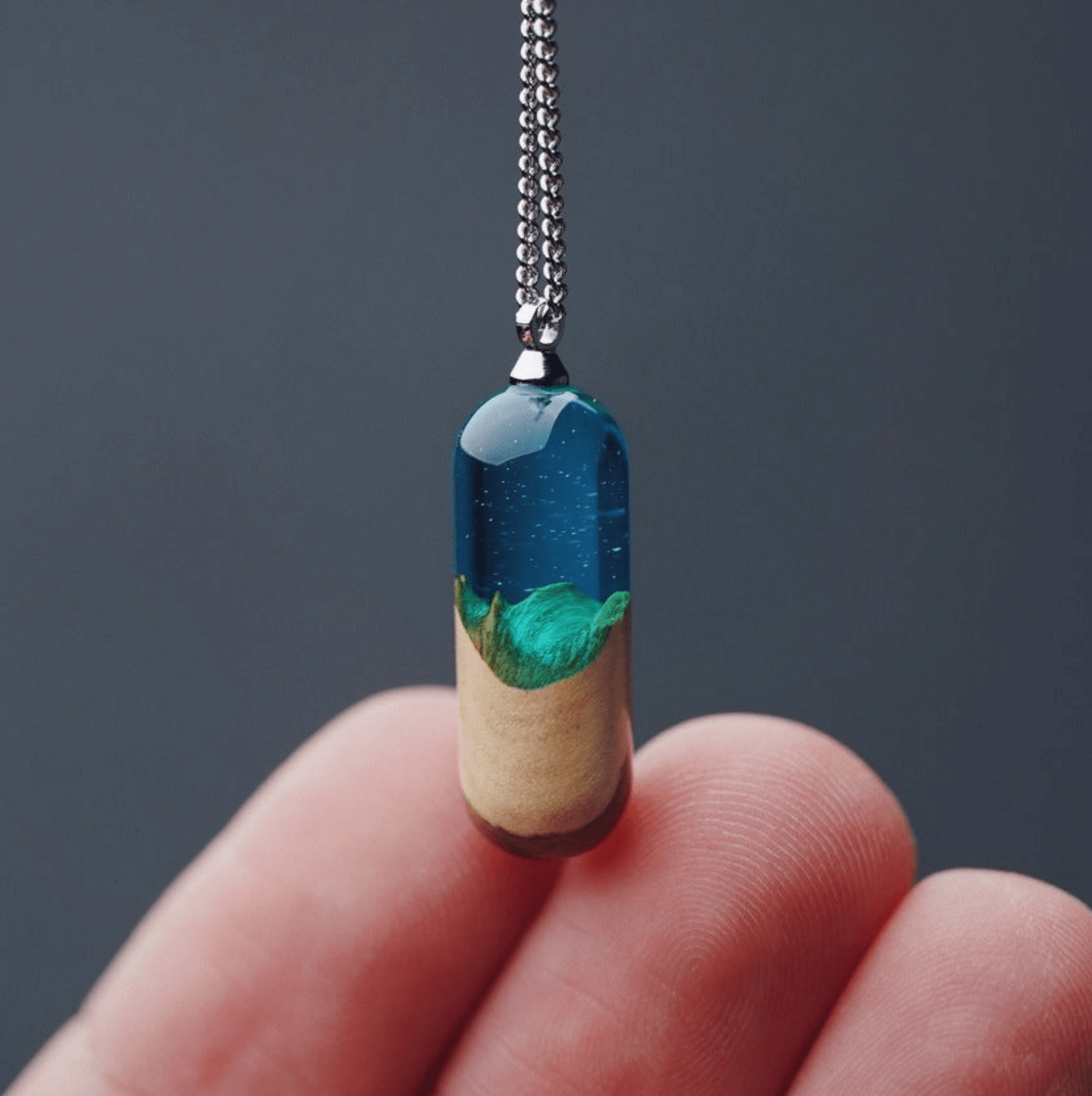 Trendy jewelry collection featuring a unique pendant that combines blue resin and greenery, held in a hand.