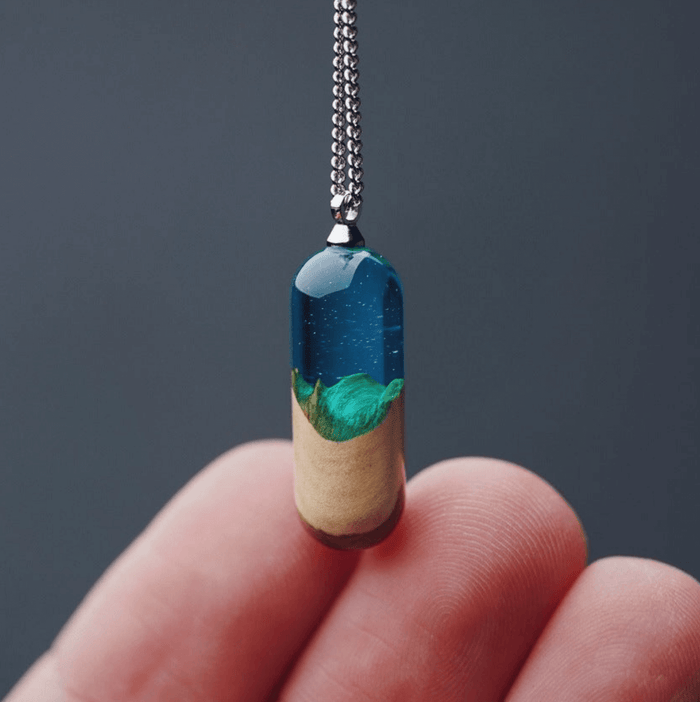 Trendy jewelry collection featuring a unique pendant that combines blue resin and greenery, held in a hand.