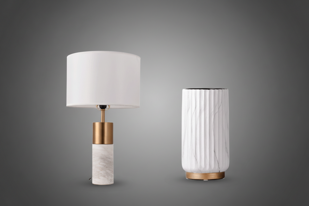 Table lamp with white shade and marble base next to a cylindrical white vase on a white background