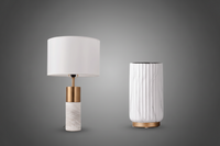 Table lamp with white shade and marble base next to a cylindrical white vase on a white background