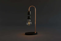 A levitating smart lamp with a transparent bulb, silver metal parts, and a vintage wood base, illuminated and floating above a black surface.